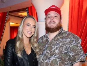 Luke Combs in a camo shirt and red hat and Nicole in a black jacket.
