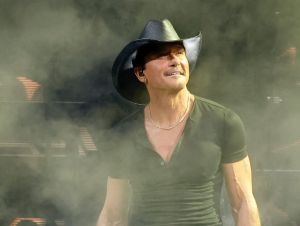 Tim McGraw performing on stage in Nashville wearing a black t-shirt and cowboy hat.