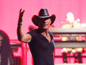 Tim McGraw on stage in a black shirt and cowboy hat.