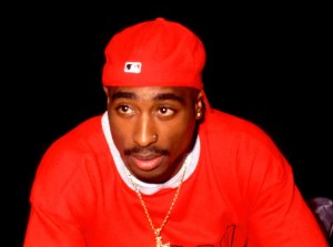 Tupac Shakur wearing a red shirt and red hat sitting down.