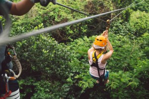 Female in a yellow helmet takes off on a zipline over trees. North Carolina zipline course.