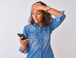 woman using smartphone standing over isolated white background stressed with hand on head, shocked with shame and surprise face, angry and frustrated. Fear and upset for mistake.