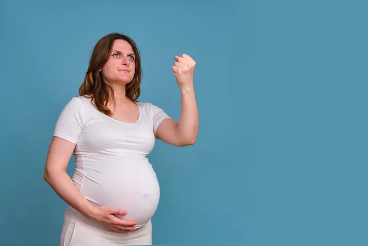 Portrait of a pregnant woman with a threatening fist gesture on a blue background