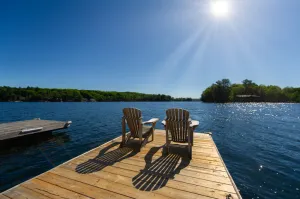 Cottage life - Sunrise on two empty Adirondack chairs sitting on a dock on a lake. Luxury waterfront cottages