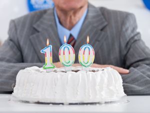 Man with a birthday cake with candles that say "100." As it turns out, people who live to 100 have certain things in common.