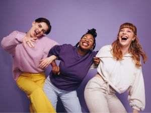 Vibrant multiethnic friends dancing with laughter and having fun in a studio. Group of happy female friends celebrating and having a good time against a purple background