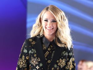 Carrie Underwood is posing in a black patterned suit.