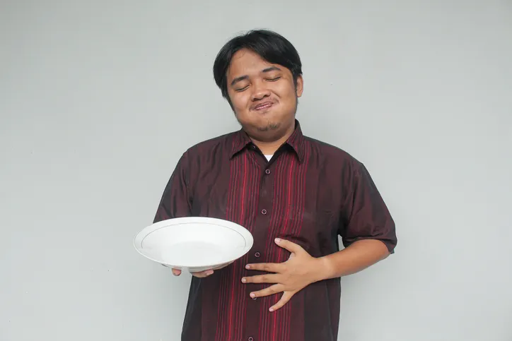 Asian young man holding empty plate and her stomach with happy and full expression.